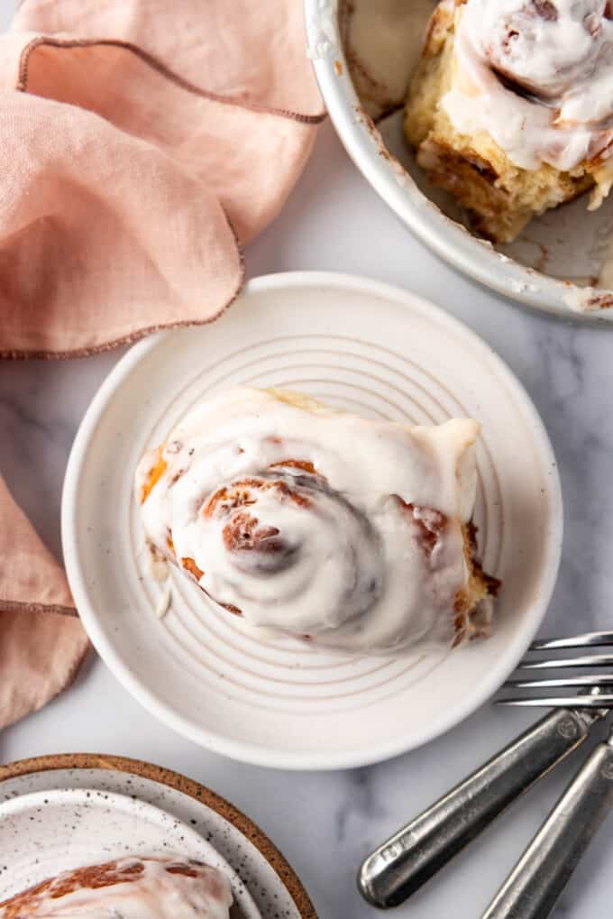 An overhead image of a cinnamon roll on a white plate next to a pink linen napkin.