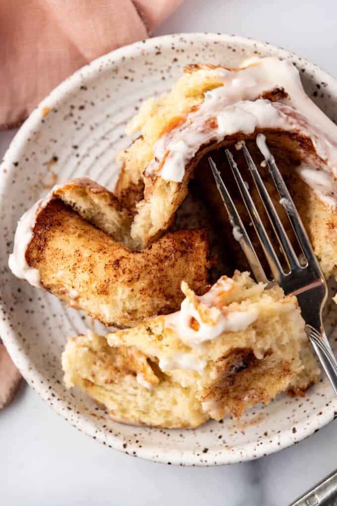 A close image of a cinnamon roll that has been torn apart with a fork to show the soft center.