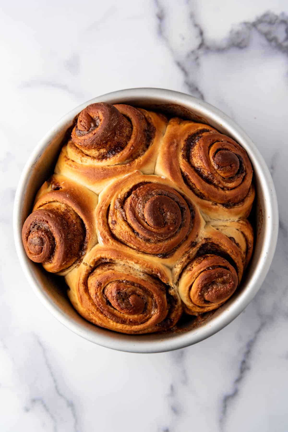 An overhead image of baked cinnamon rolls in a round pan without frosting.