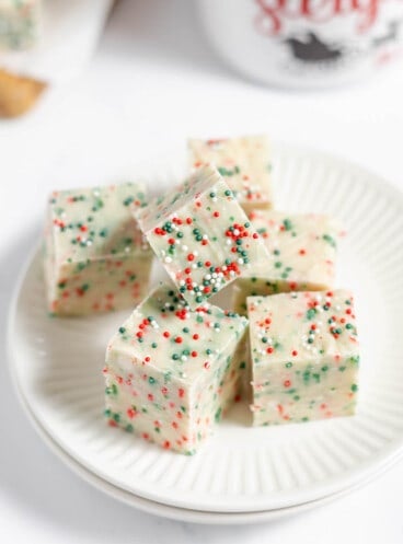 Squares of sugar cookie fudge stacked on a plate.