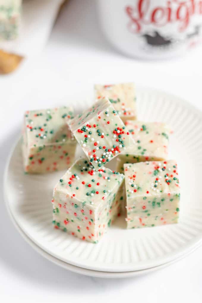 Squares of sugar cookie fudge stacked on a plate.