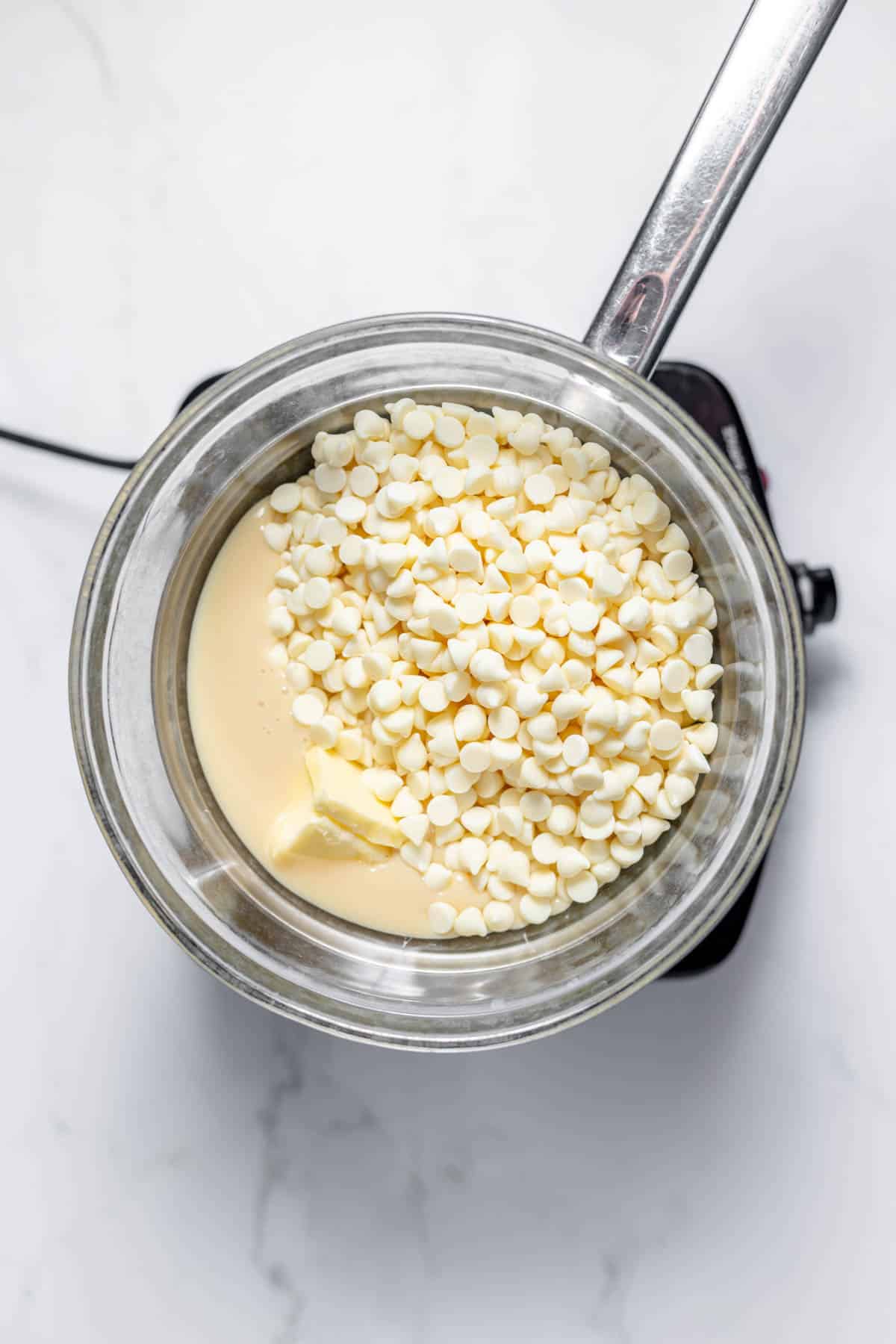 Melting butter, white chocolate chips, and sweetened condensed milk in the top of a double boiler.