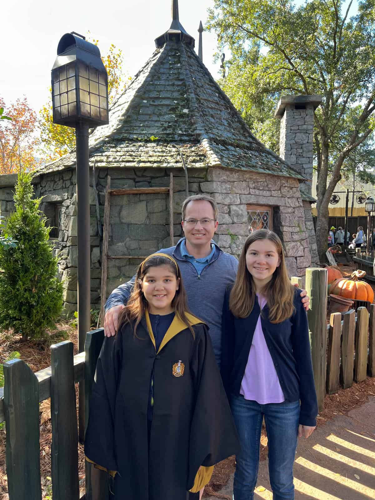 A dad and two daughters outside of Hagrid's hut.