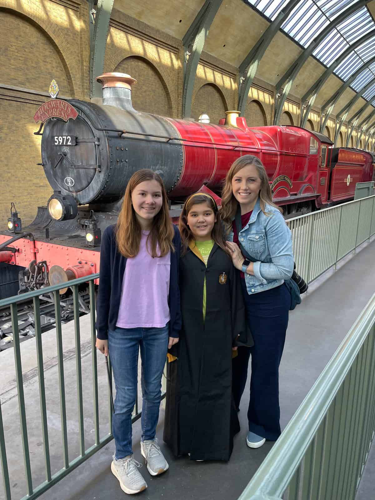 An image of a mom and two daughters in front of the Hogwarts Express on platform 9 and ¾ at King's Cross Station.