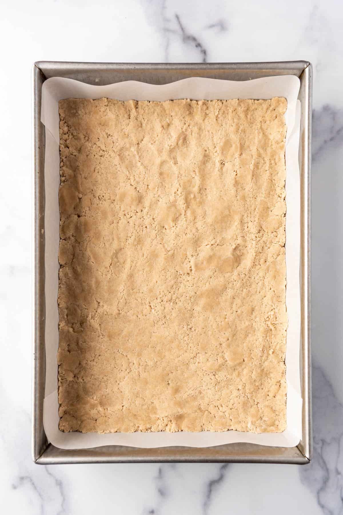 Pressing shortbread crust into a rectangular baking pan.