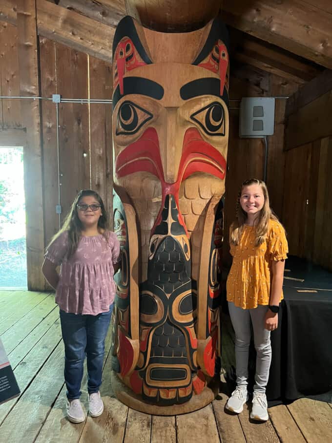 Two kids next to a totem pole.