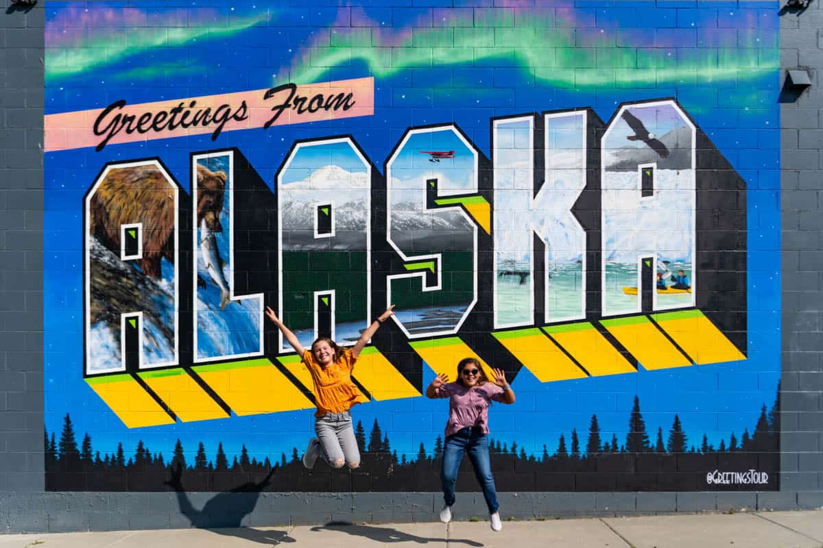 Two kids jumping in front of the Alaska mural sign in Anchorage.