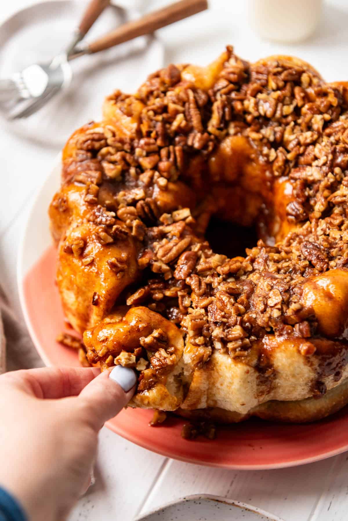 An image of a hand pulling apart a piece of caramel pecan monkey bread.