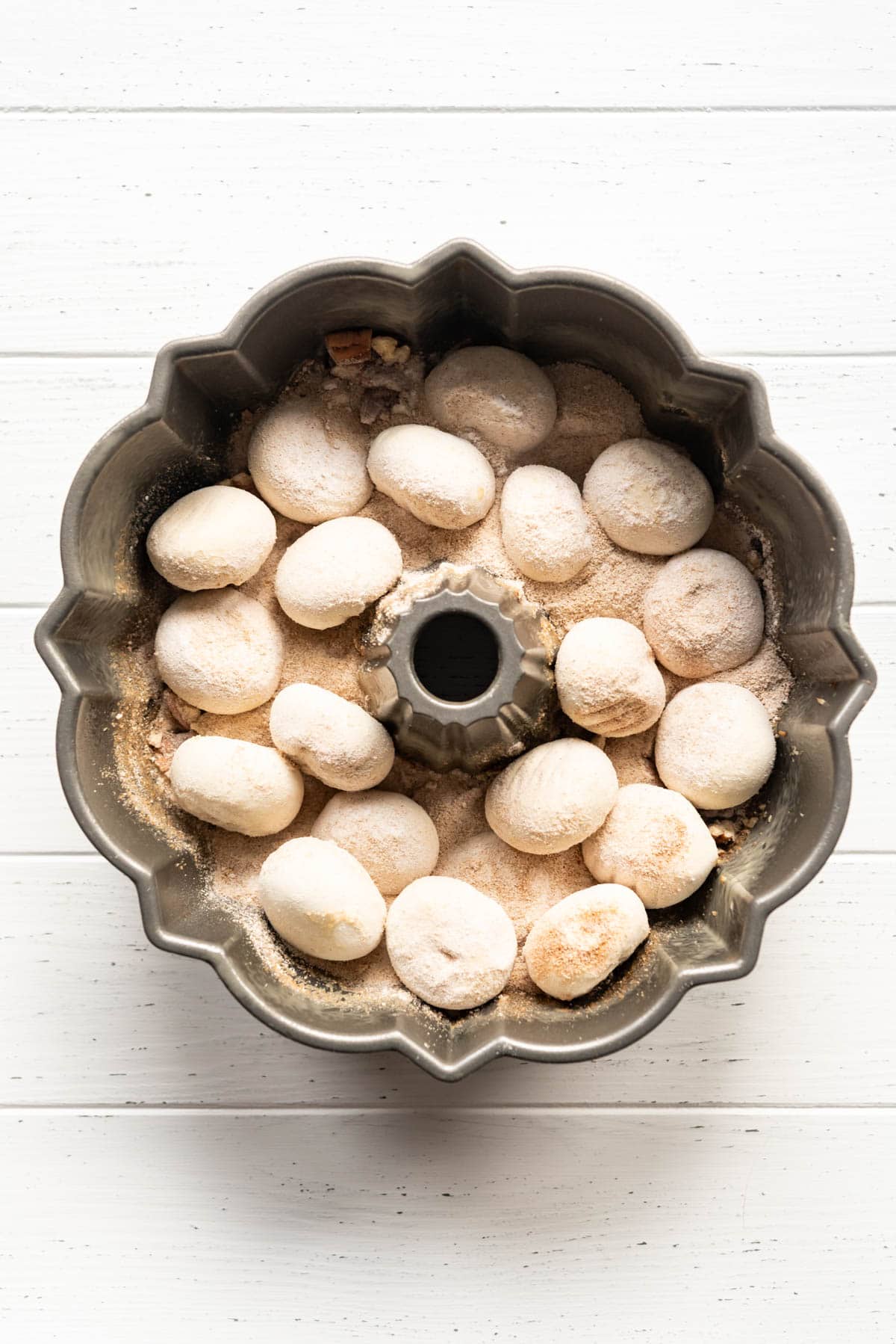 Adding frozen roll dough, cinnamon, brown sugar, and butterscotch pudding to a bundt pan.