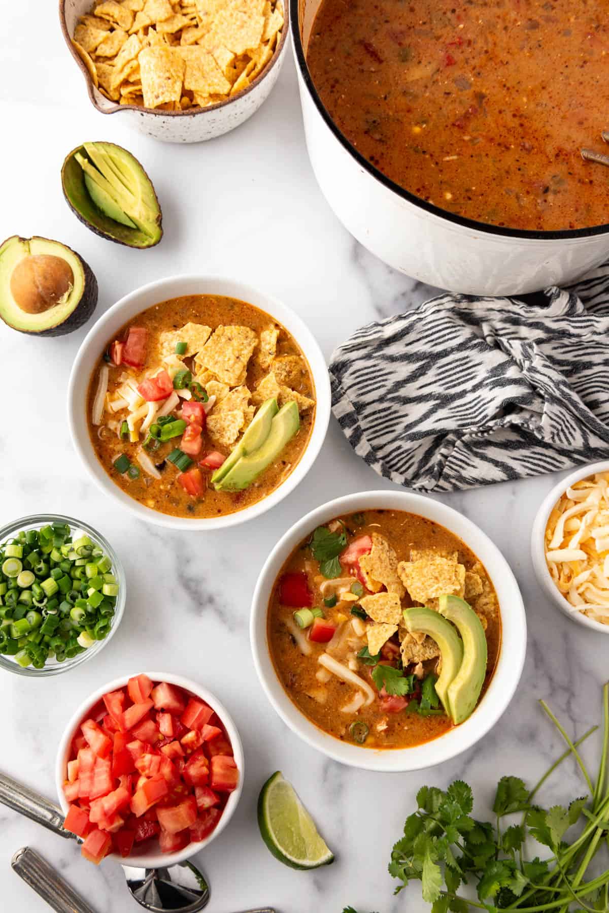 Two bowls of chicken tortilla soup next to toppings and a big pot of the soup.