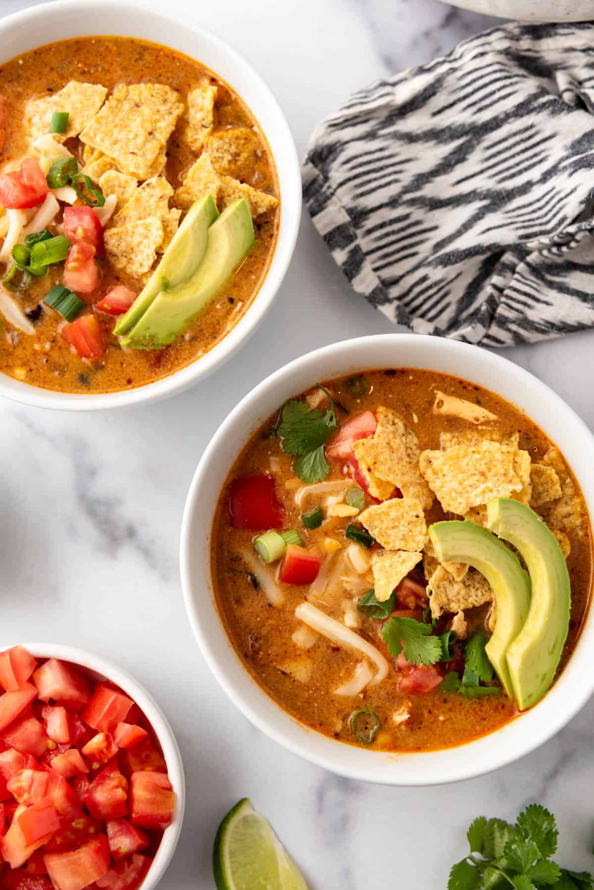 An overhead image of bowls of chicken tortilla soup with fixings on top and a cloth napkin to the side.