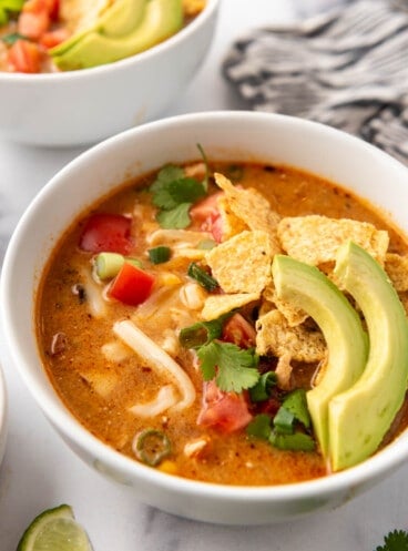 A bowl of homemade chicken tortilla soup with tortilla chips and sliced avocados on top.