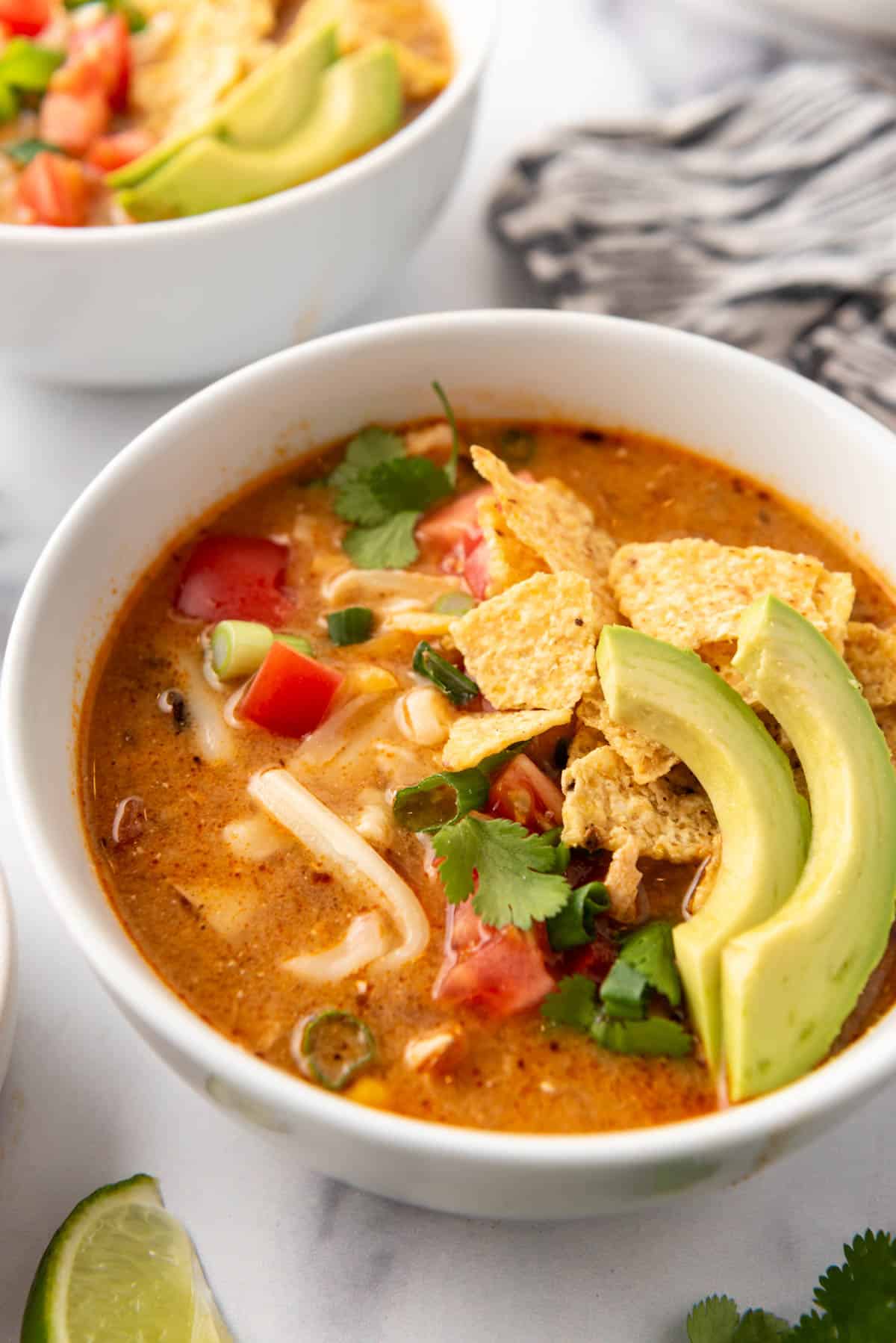 A bowl of homemade chicken tortilla soup with tortilla chips and sliced avocados on top.