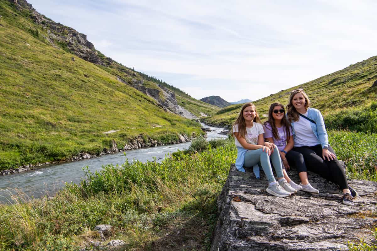 A mom and two daughters sitting in front of the Savage River in Denali National Park.