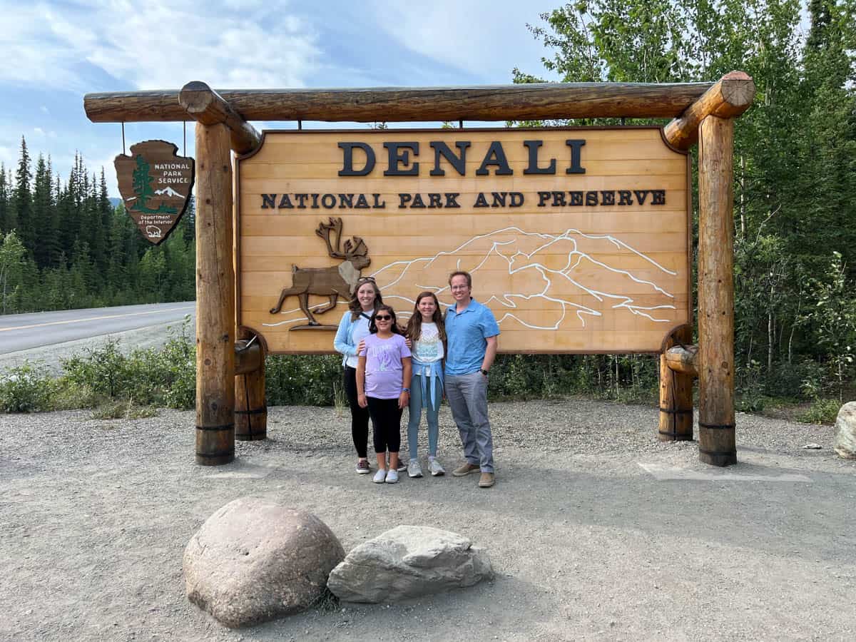 An image of a family of four in front of the entrance to Denali National Park sign.