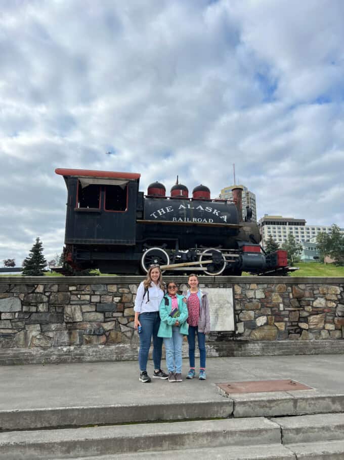 A mom and two kids in front of a train engine.