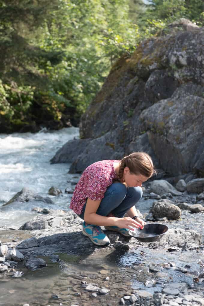 A girl looking in a pan for gold flakes next to a river in Girdwood, Alaska.