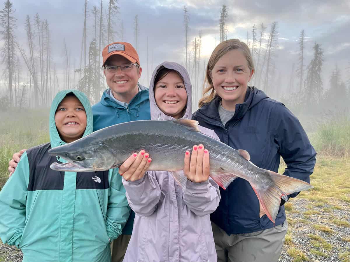 A family of four around a girl holding a sockeye salmon.