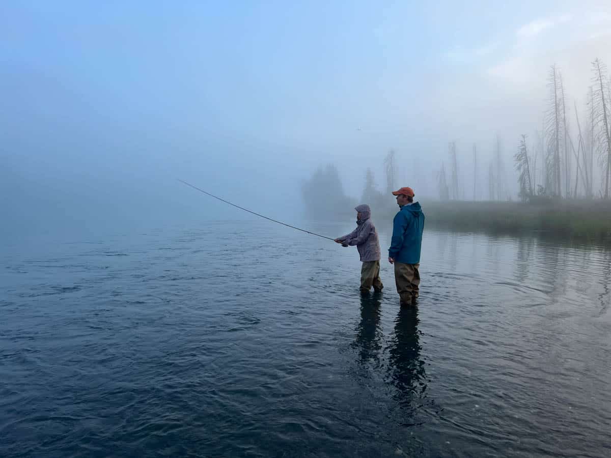 A dad and his daughter fishing on the Kenai River in Soldotna, Alaska early in the morning in foggy weather.