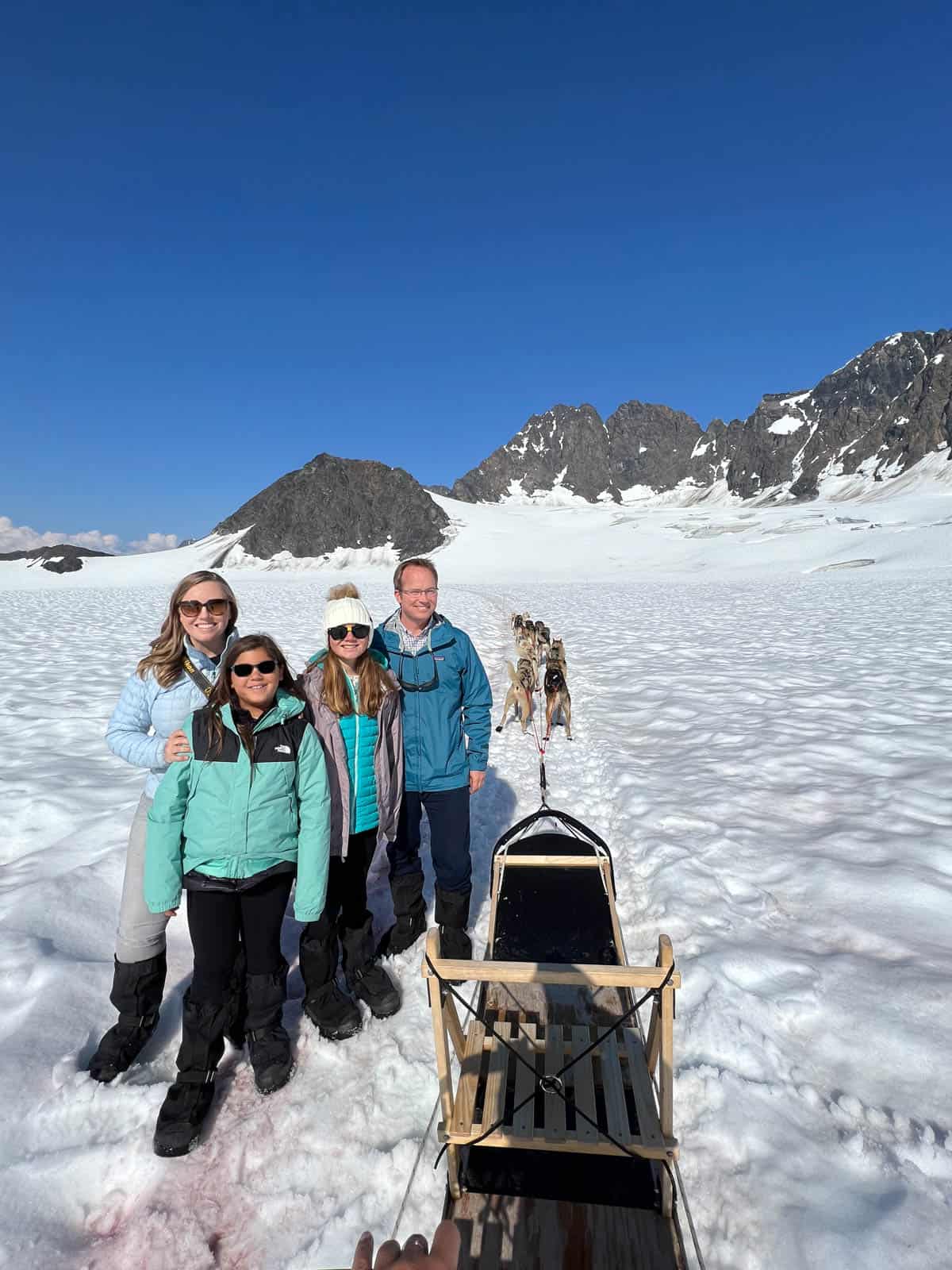 A family in front of a dog sled on a glacier.