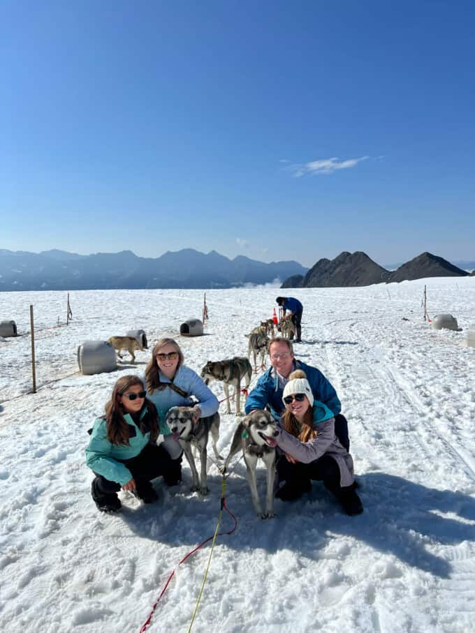 A family with a team of sled dogs in the snow.