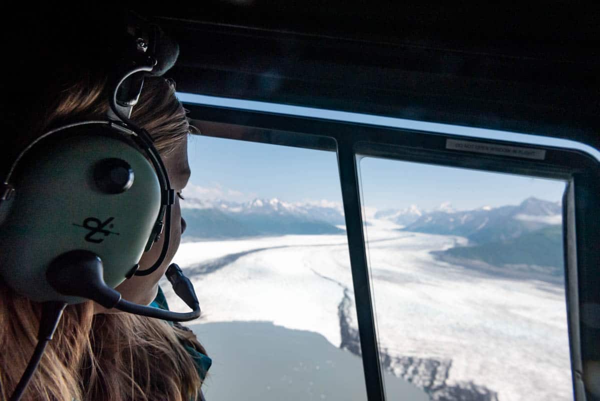 A girl looking out the window of a helicopter at a glacier in Alaska.