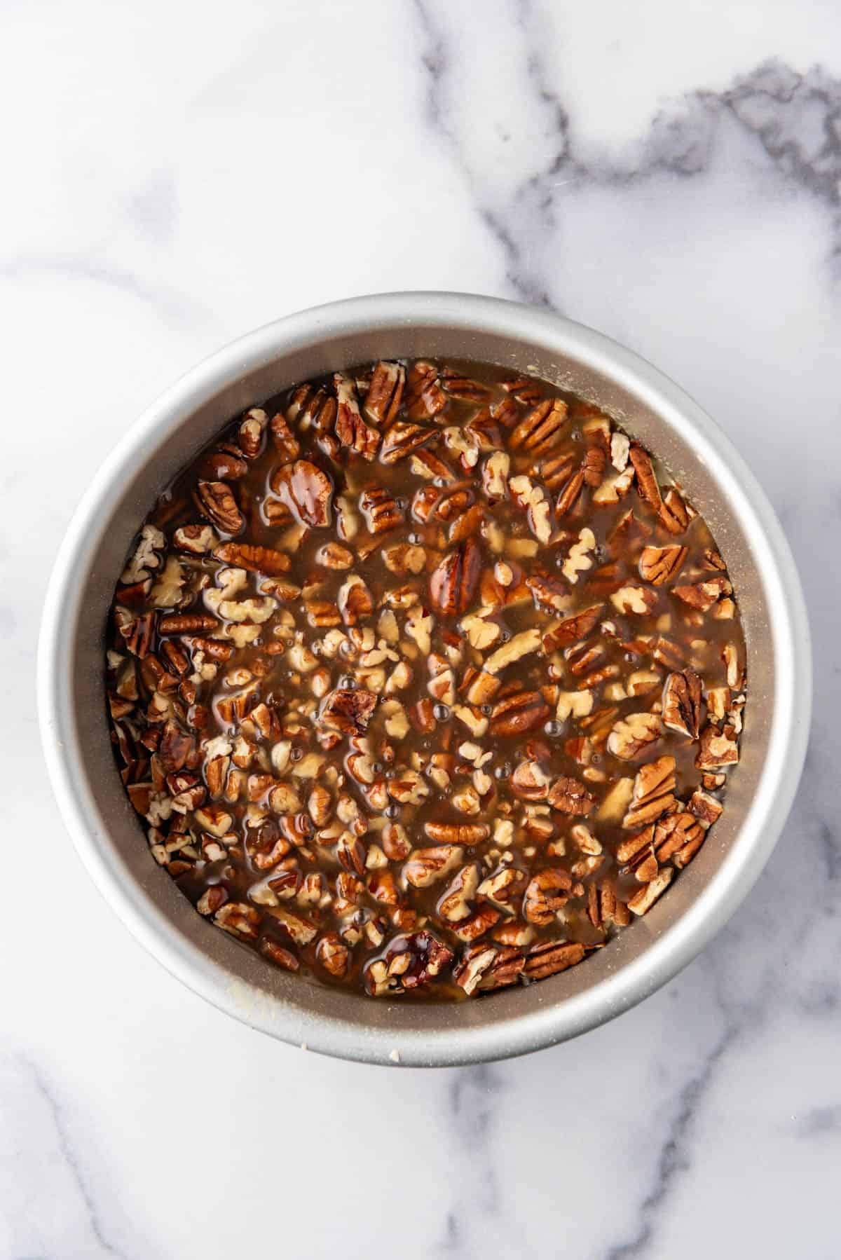 Chopped pecans in the bottom of an  8-inch baking pan with homemade caramel ingredients.