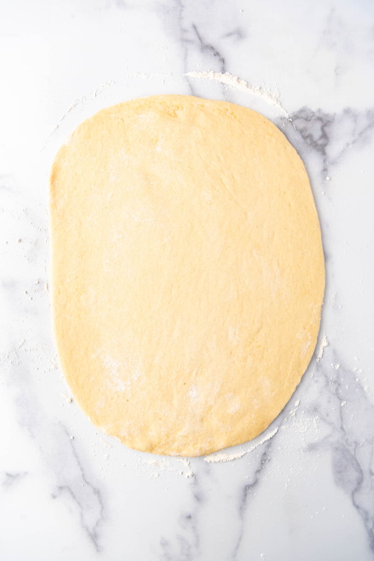Rolling out cinnamon roll dough on a clean white marble surface.