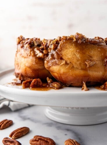 A close up image of a side view of caramel pecan sticky buns on a white cake stand.