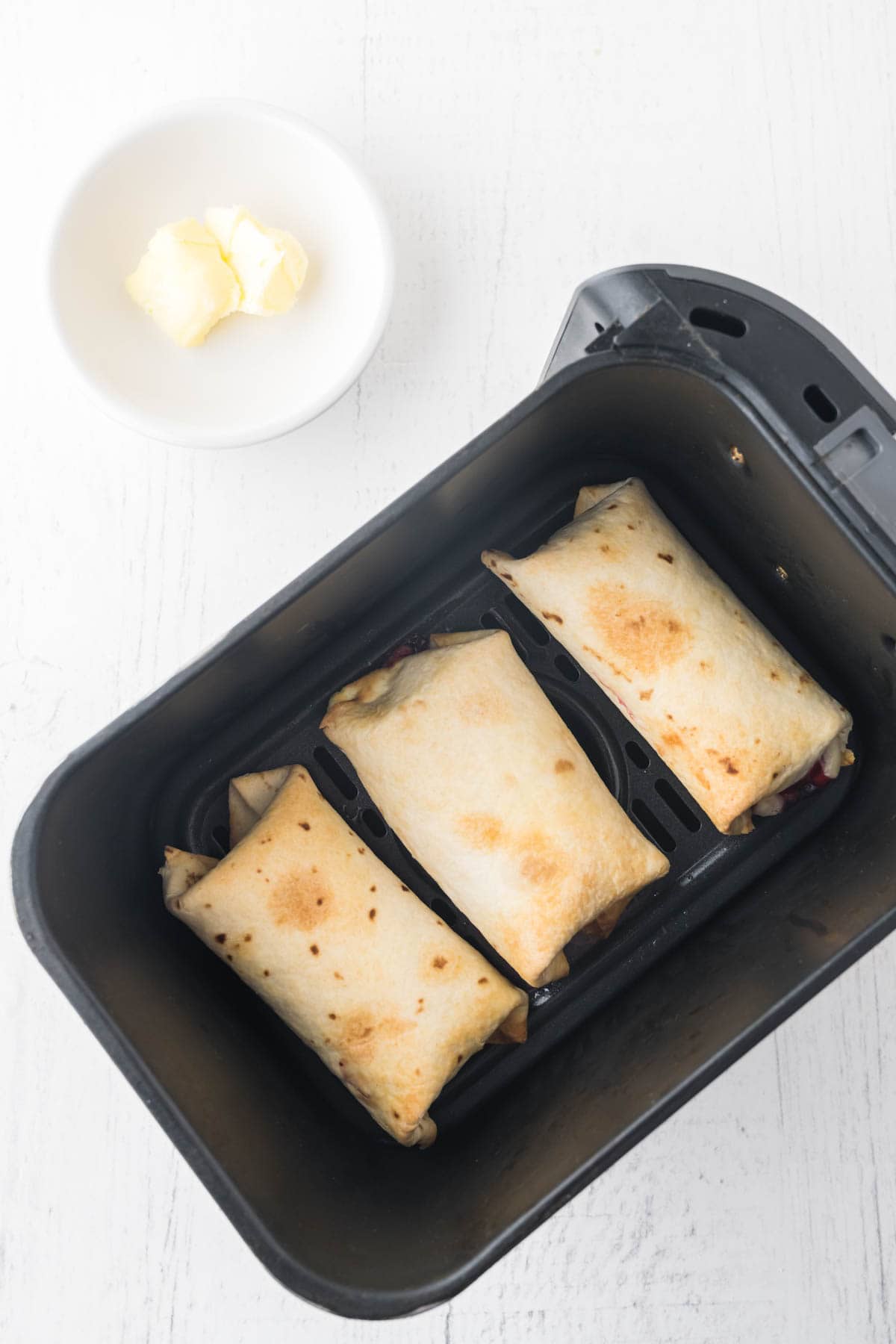 Cooked air fryer cheesecake chimichangas in an air fryer basket.