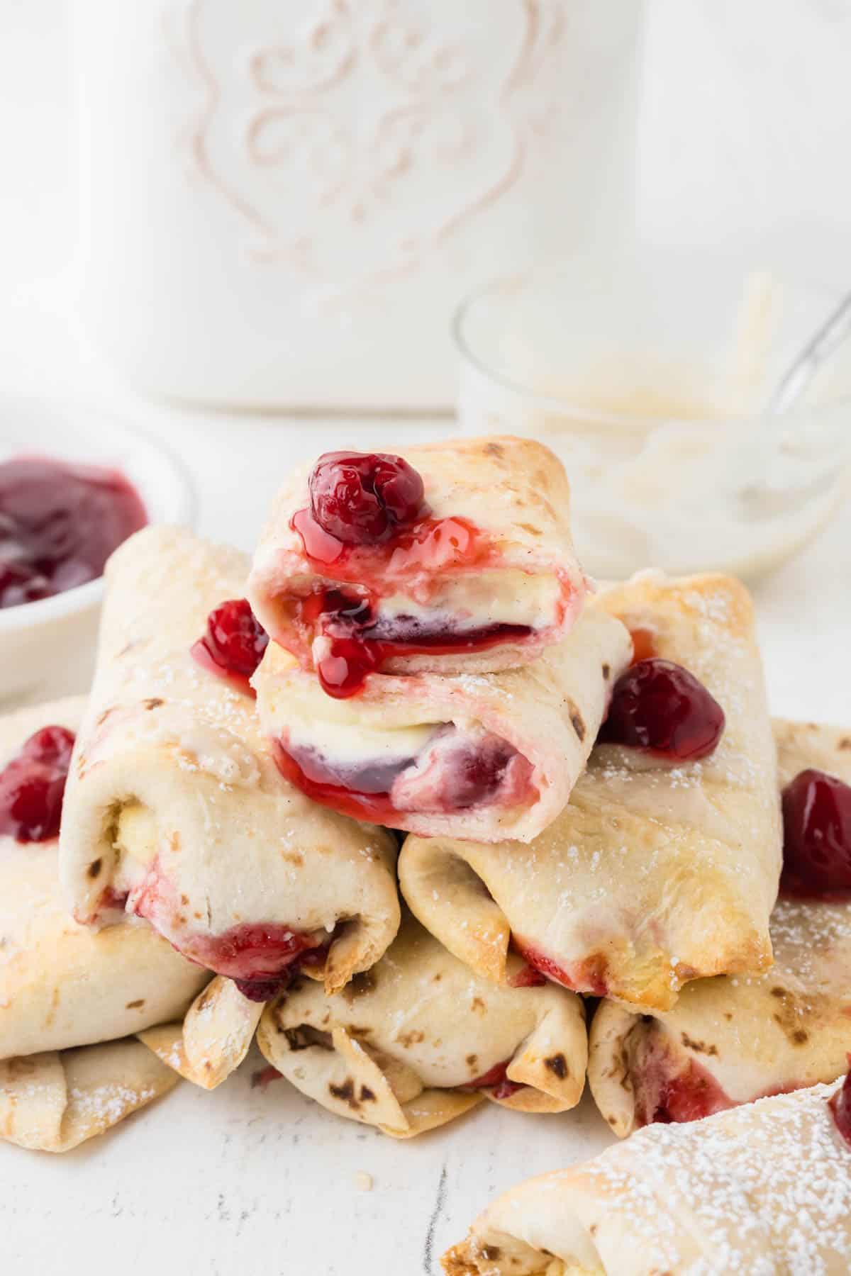 An image of air fryer cherry cheesecake chimichangas stacked in a pile with the top one cut in half.