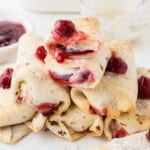 An image of air fryer cherry cheesecake chimichangas stacked in a pile with the top one cut in half.