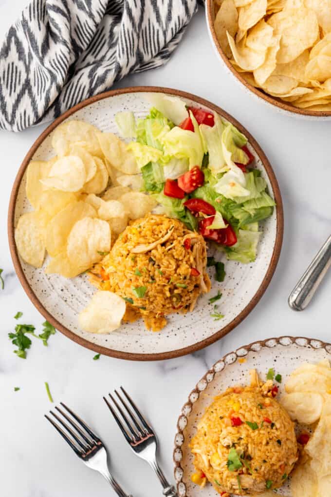 An overhead image of a plate of arroz con pollo with potato chips and a simple salad.