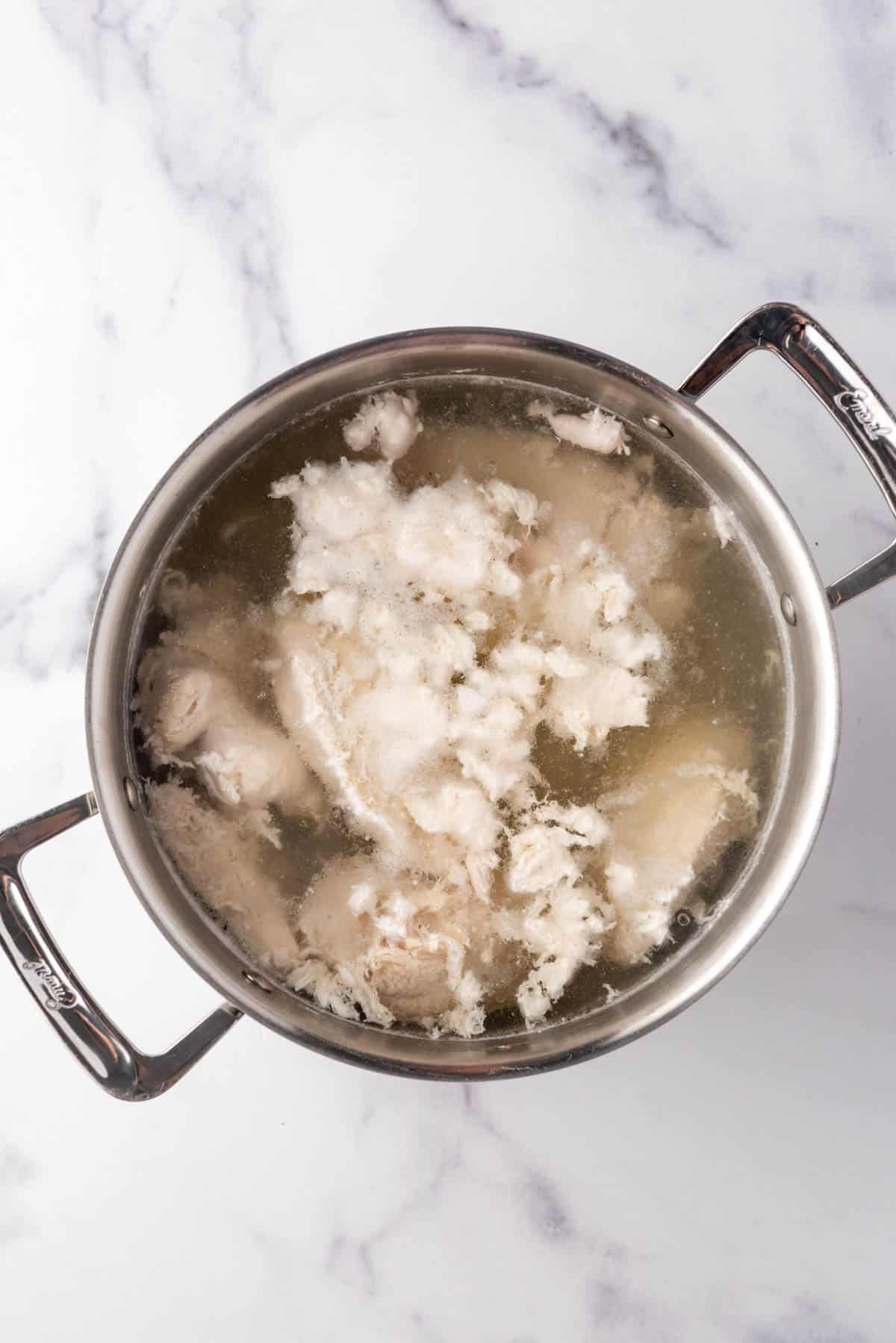 Chicken breasts boiling in a large pot of water.