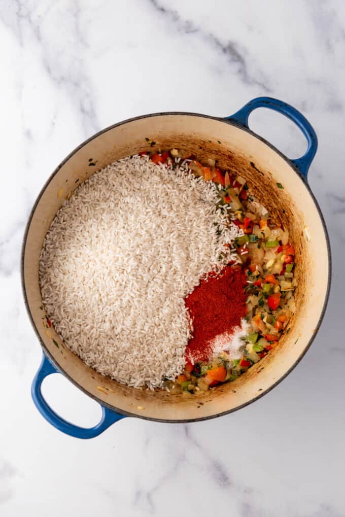 Adding rice and achiote powder to a large pot for arroz con pollo.