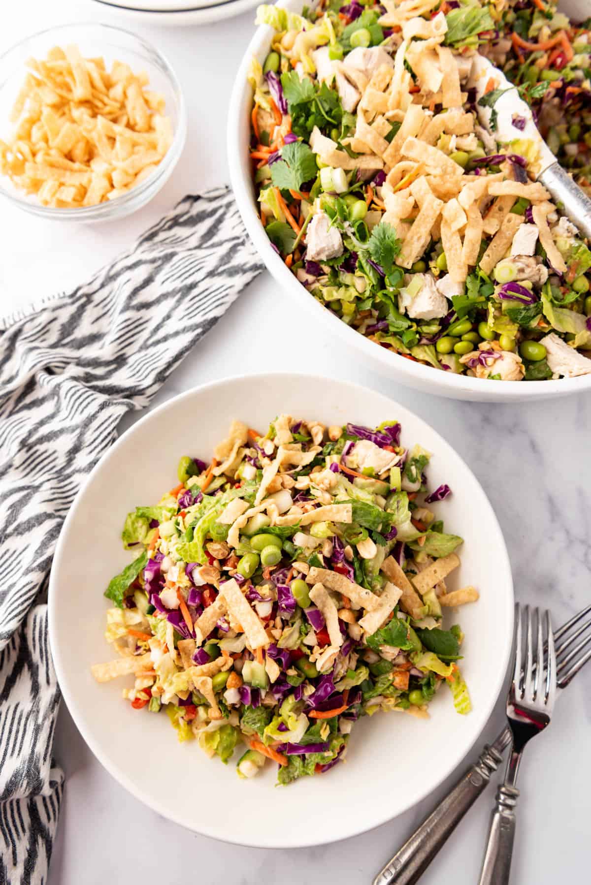 An overhead image of a plate of Thai chicken salad next to a big bowl of the rest of the salad.