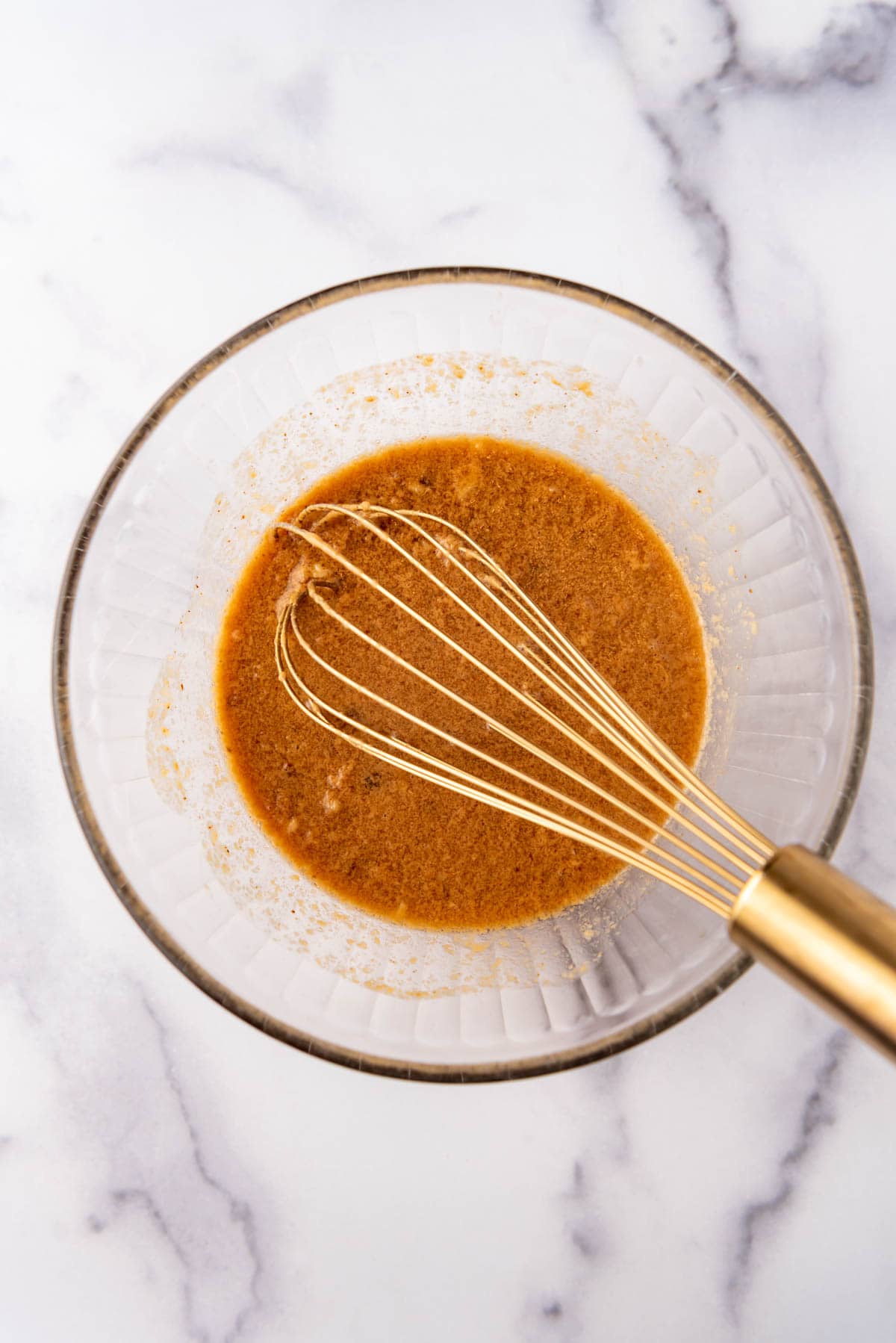 Finished peanut dressing in a bowl with a brass whisk.