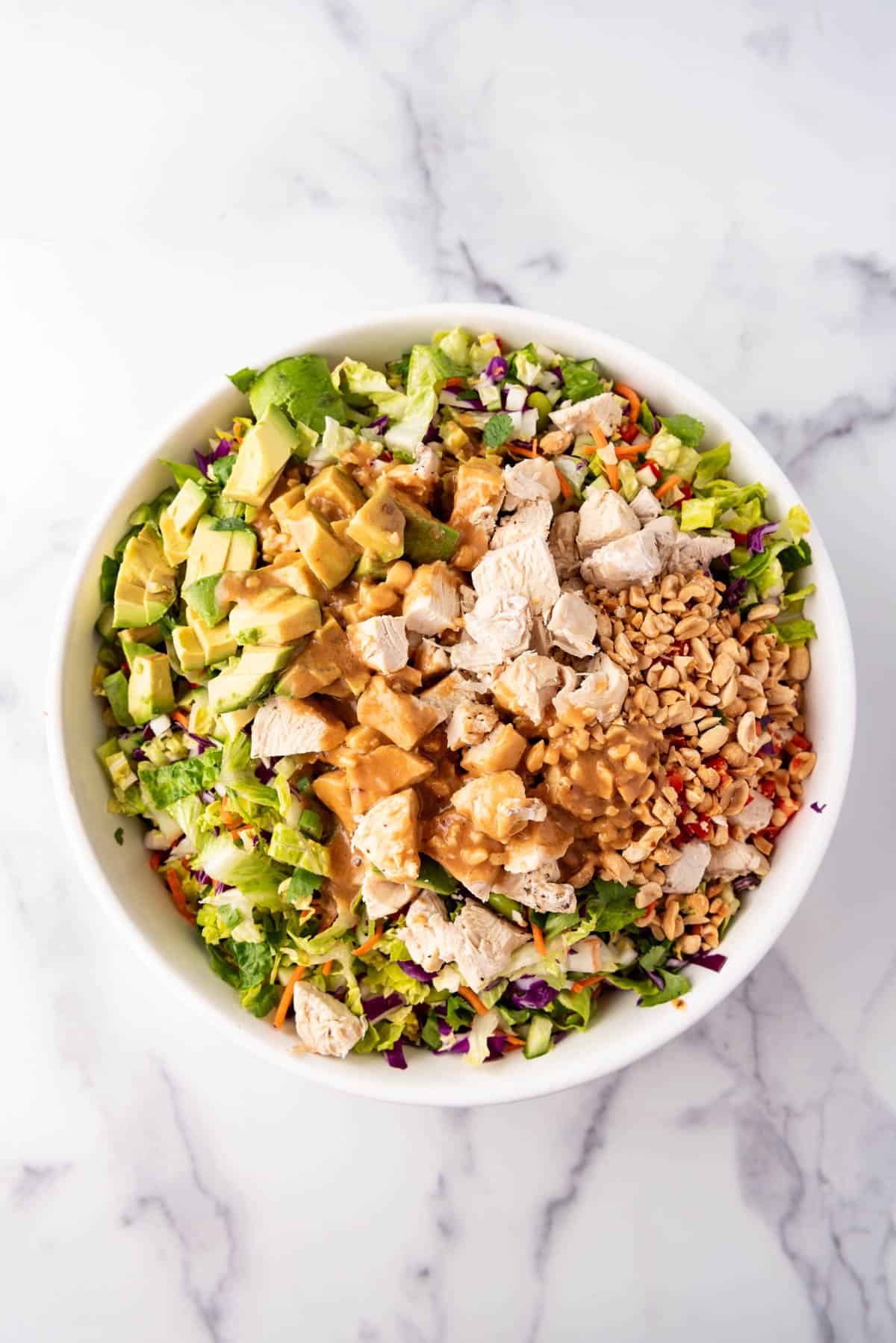 An overhead image of a bowl of Thai chicken salad with peanut dressing poured on top before tossing it.