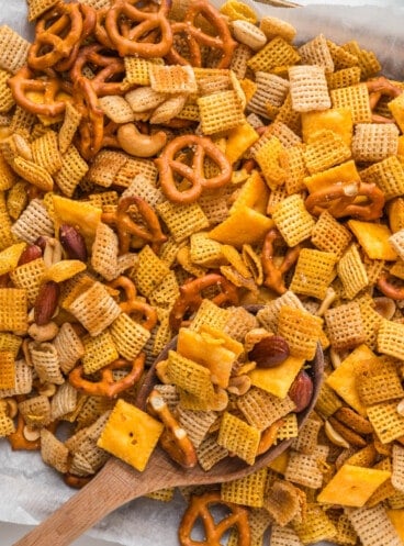 An overhead image of a wooden spoon in a pan of homemade chex mix.