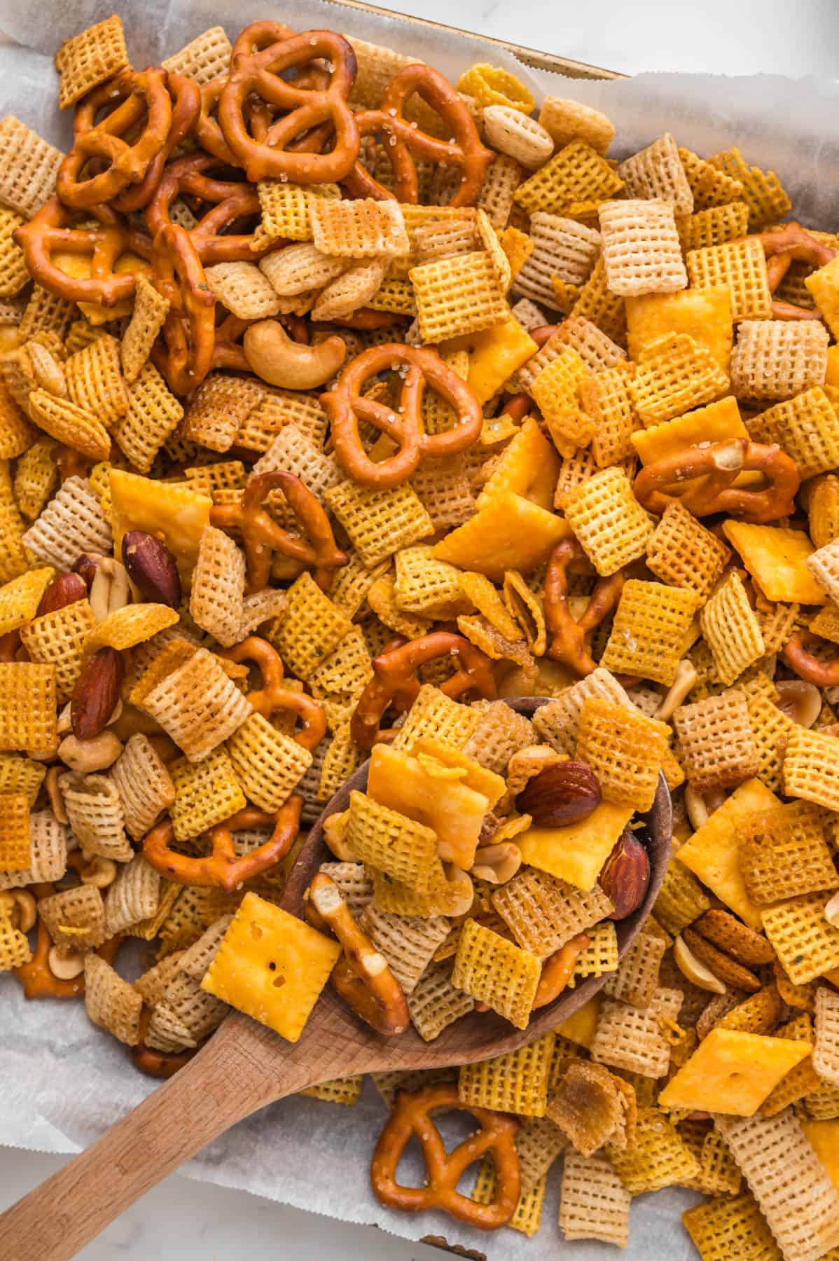 An overhead image of a wooden spoon in a pan of homemade chex mix.