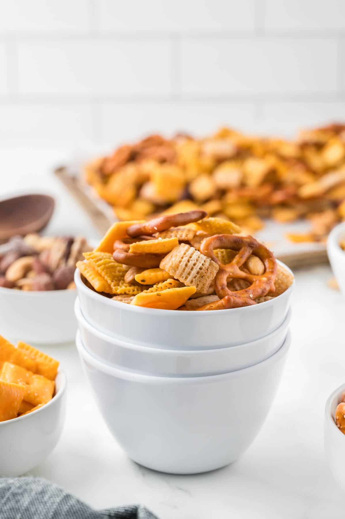 An image of stacked white bowls holding chex mix.