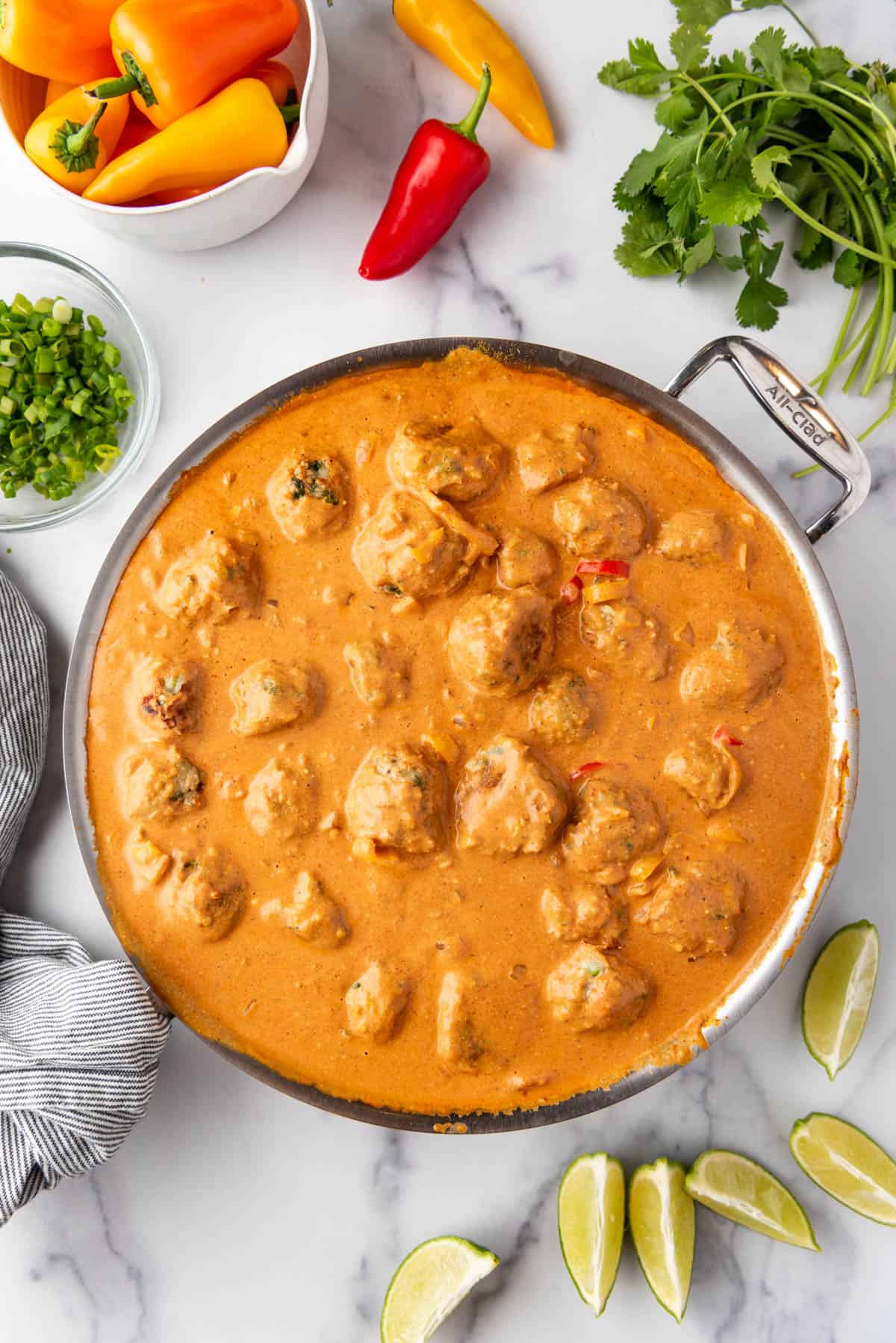 An overhead image of a pan of chicken meatballs in creamy coconut curry sauce surrounded by fresh vegetables.