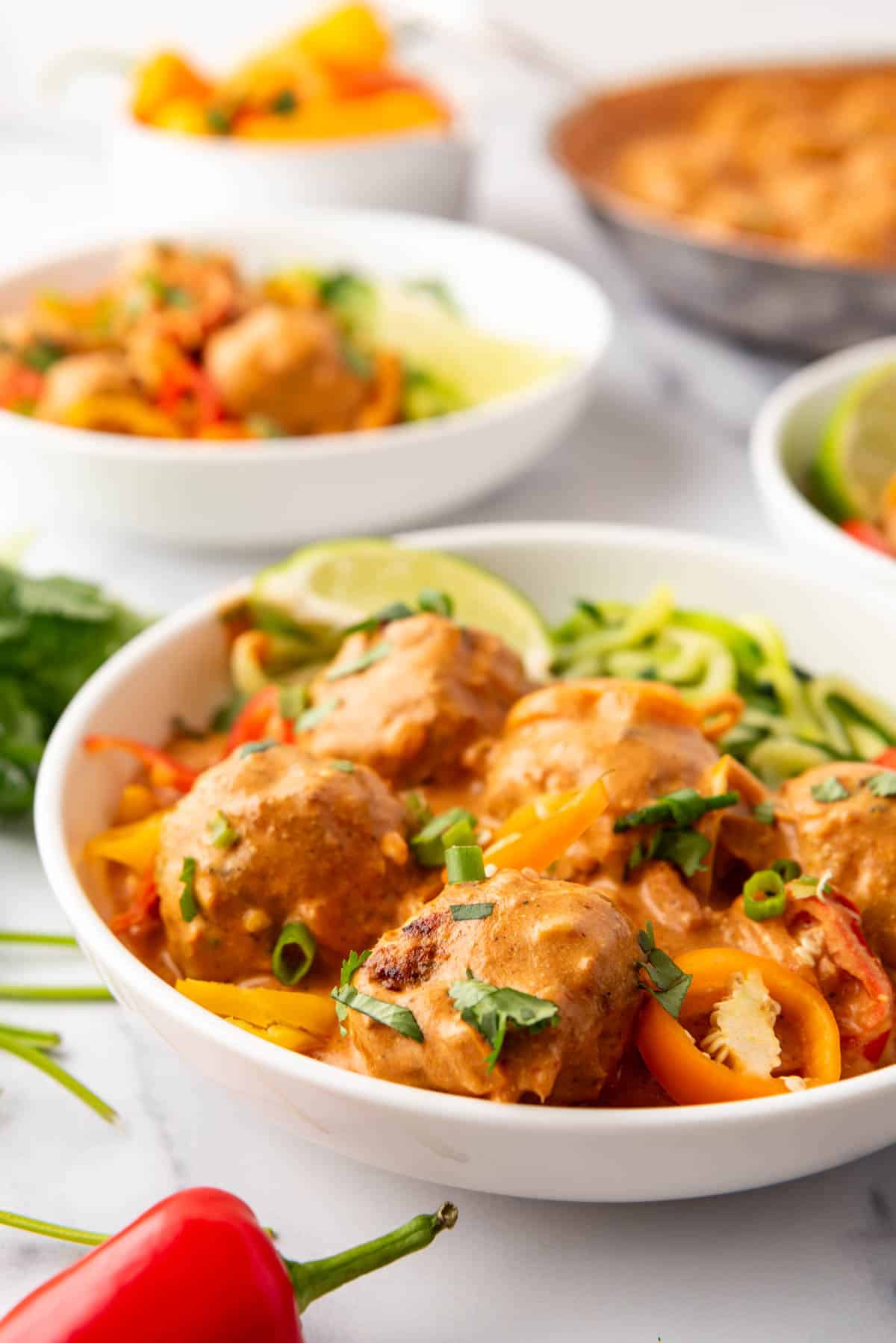 White pasta bowls of zoodles with coconut curry chicken meatballs.