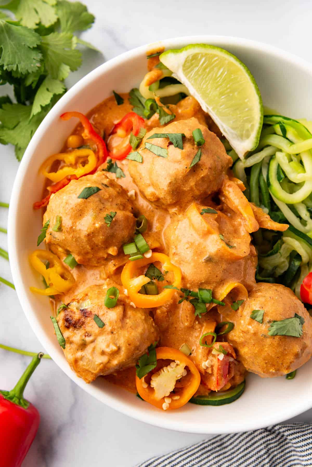 A close image of chicken meatballs in coconut curry sauce in a bowl with zoodles and a lime wedge.