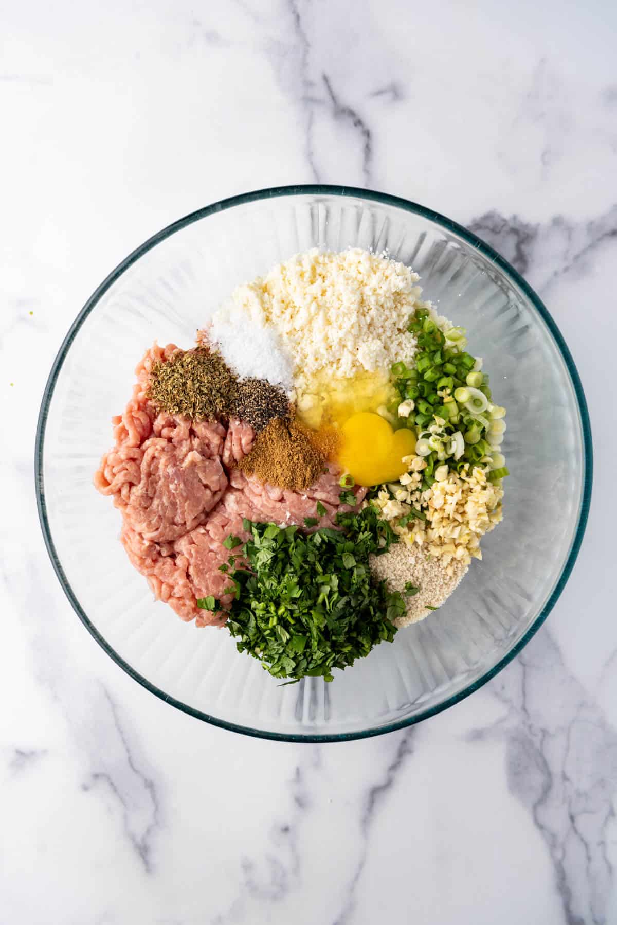 An overhead image of a bowl of ingredients for making chicken meatballs.