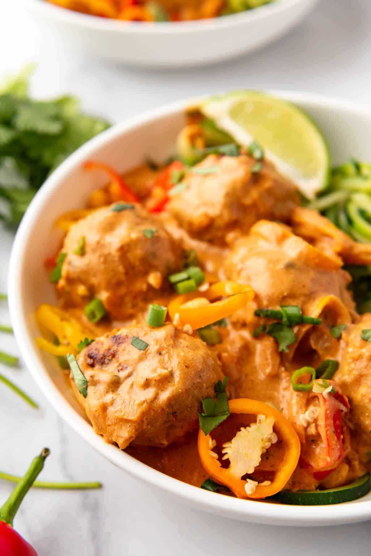 A close image of coconut curry chicken meatballs with sweet orange and red peppers.