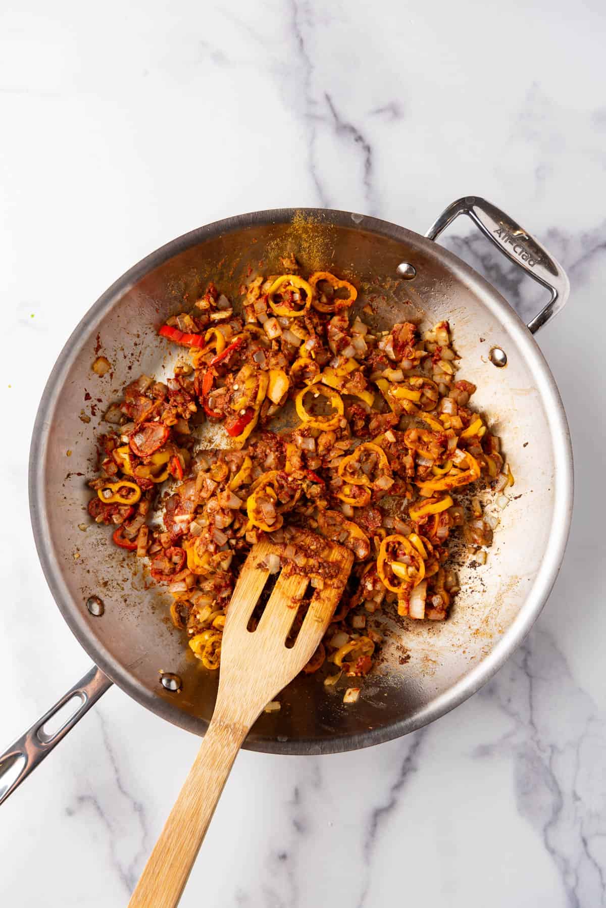 Vegetables and spices in a large pan with a wooden spatula.