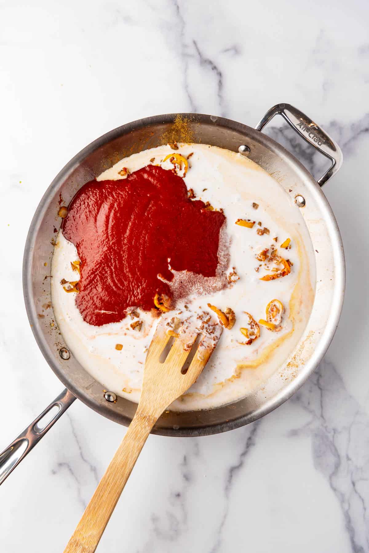 Adding tomato sauce and coconut curry to a large pan.