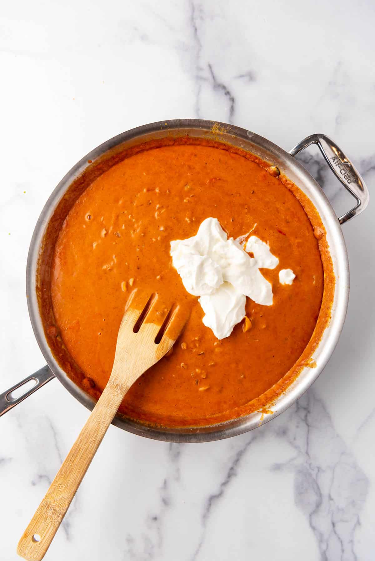 Adding Greek yogurt to a coconut curry sauce in a large pan.