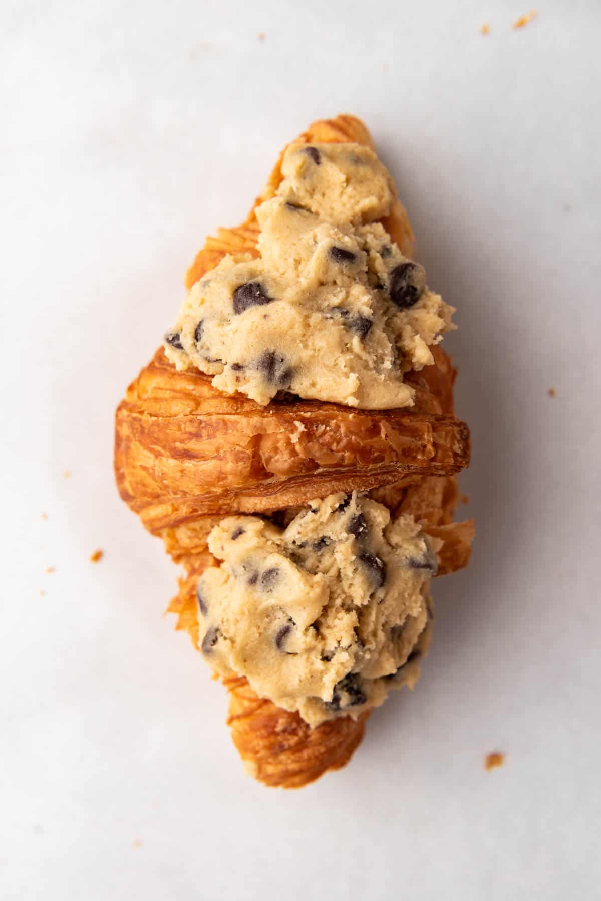 A close overhead image of a croissant with cookie dough pressed on top.
